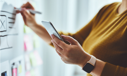 woman looking at phone and writing on board