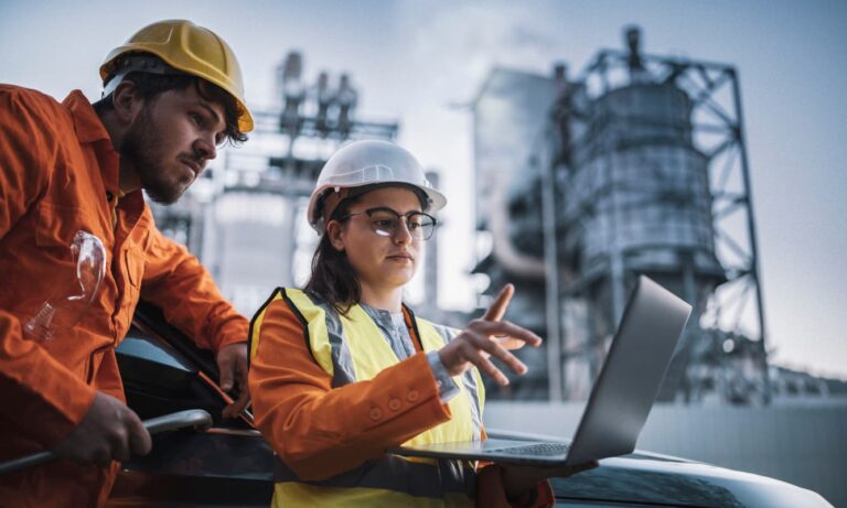Two engineers working late at a factory using a Windows 11 laptop.