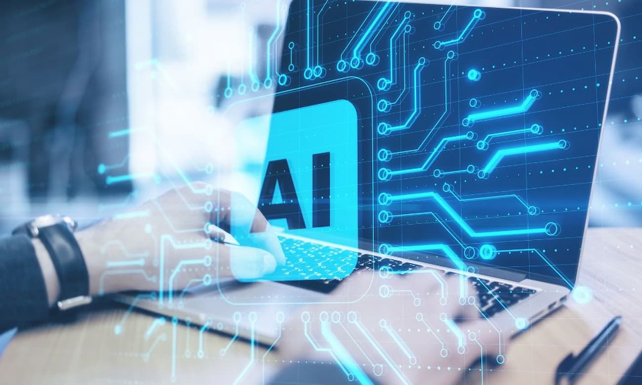 A person uses a laptop. Superimposed over their hands are the letters AI.