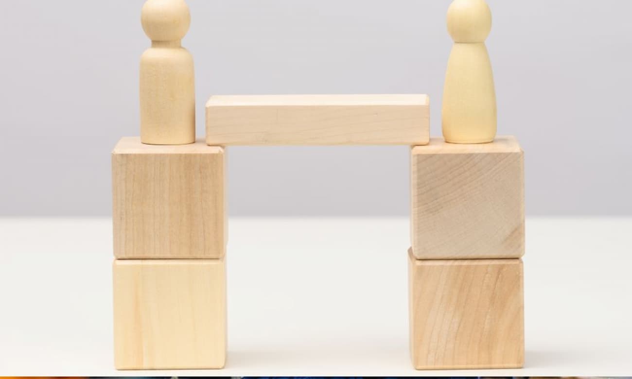 Two wooden figures on wood blocks stand on either side of a wooden bridge