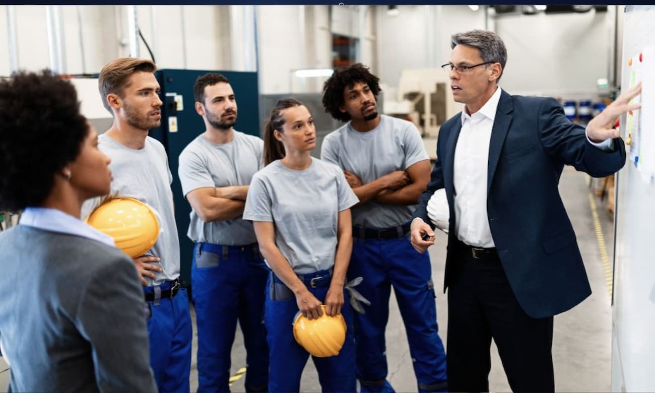 A manager for a manufacturing company gives a presentation to workers holding hard hats.